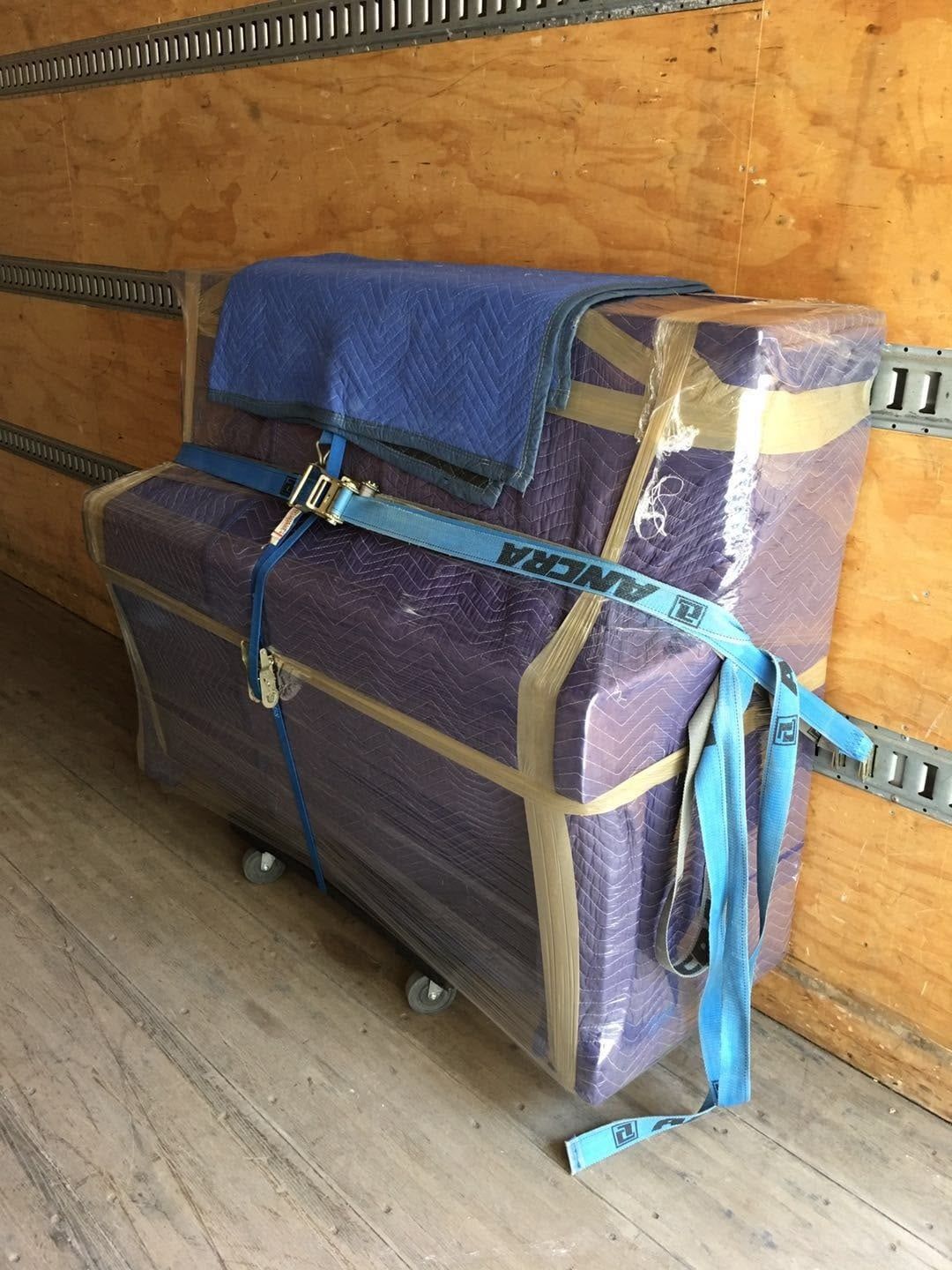 A piano wrapped in moving blankets and strapped inside our truck
