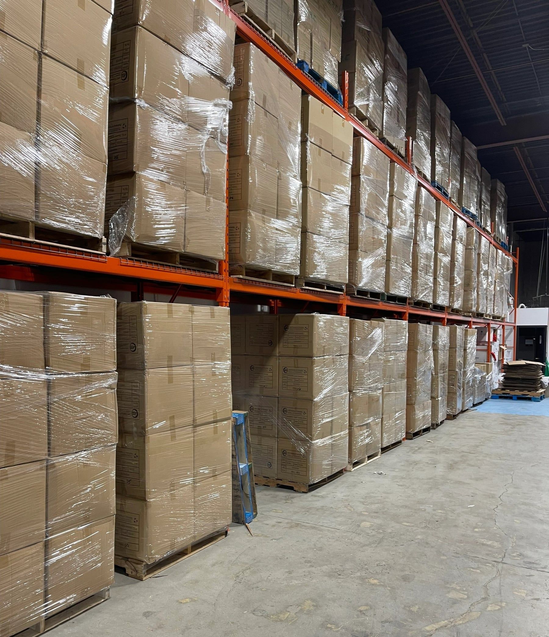 A long aisle of racked pallets, wrapped and stacked to the top beam